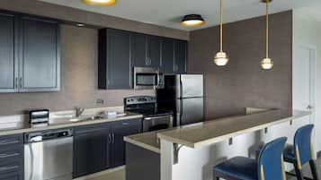 A modern kitchen with dark cabinets, stainless steel appliances, a granite countertop, and pendant lighting.