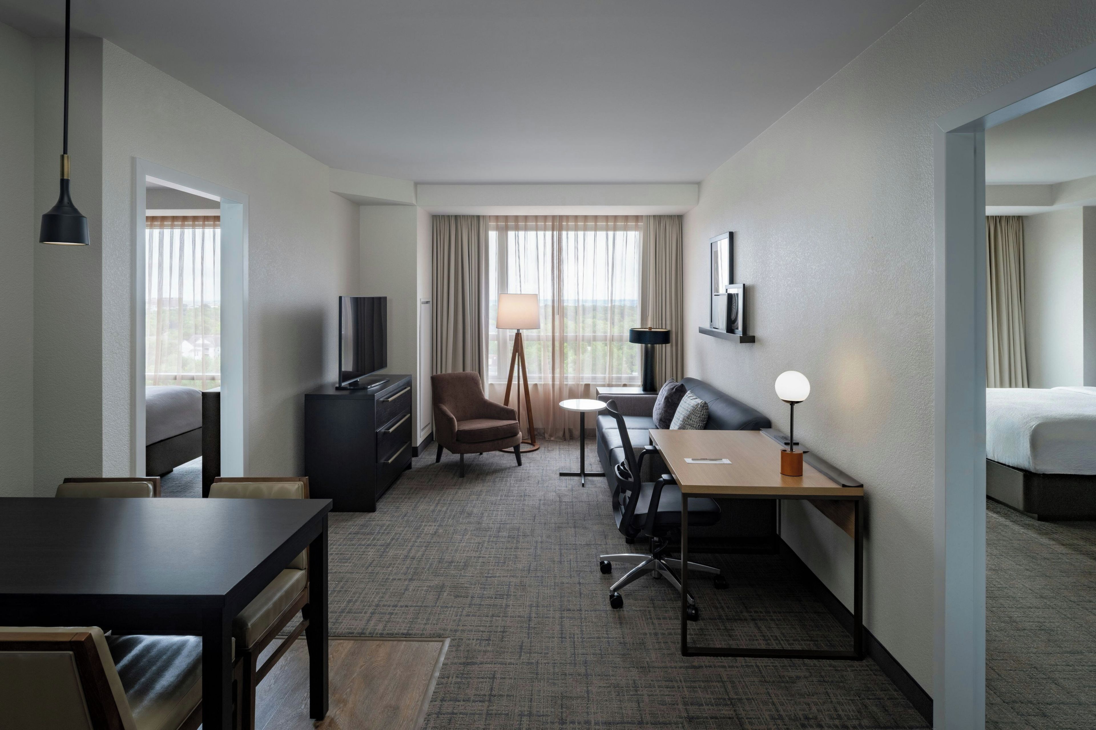 A hotel room with a bed, a desk, a chair, a television, and a lamp.