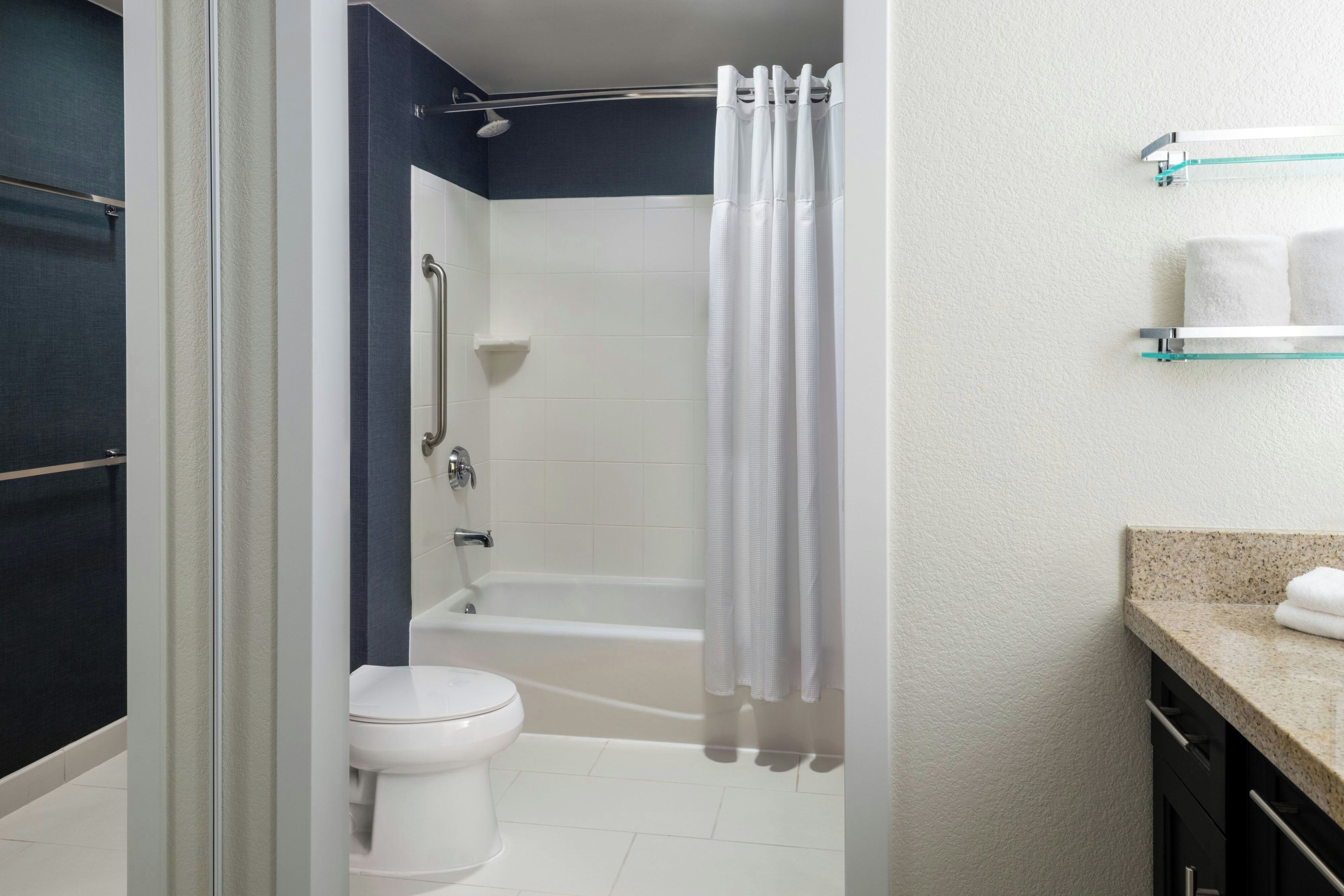A bathroom with a shower, toilet, and a glass shelf with towels.