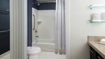 A bathroom with a shower, toilet, and a glass shelf with towels.