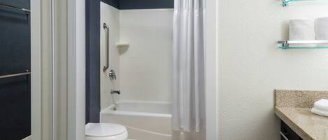 A bathroom with a shower, toilet, and a glass shelf with towels.