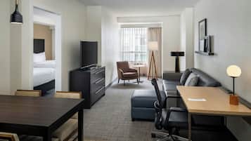 A hotel room with a bed, desk, chair, sofa, TV, lamp, and window with curtains.
