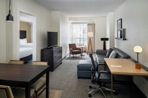 Een hotelkamer met een bed, bureau, stoel, bank, televisie, lamp en raam met gordijnen.