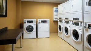 A laundry facility with multiple washing machines and dryers, a table, and a sign indicating soap and detergent options. - Residence Inn Arlington Ballston (Arlington)