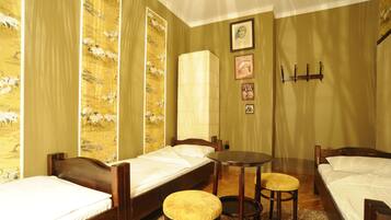 A room with two single beds, a small round table, and a stool.
