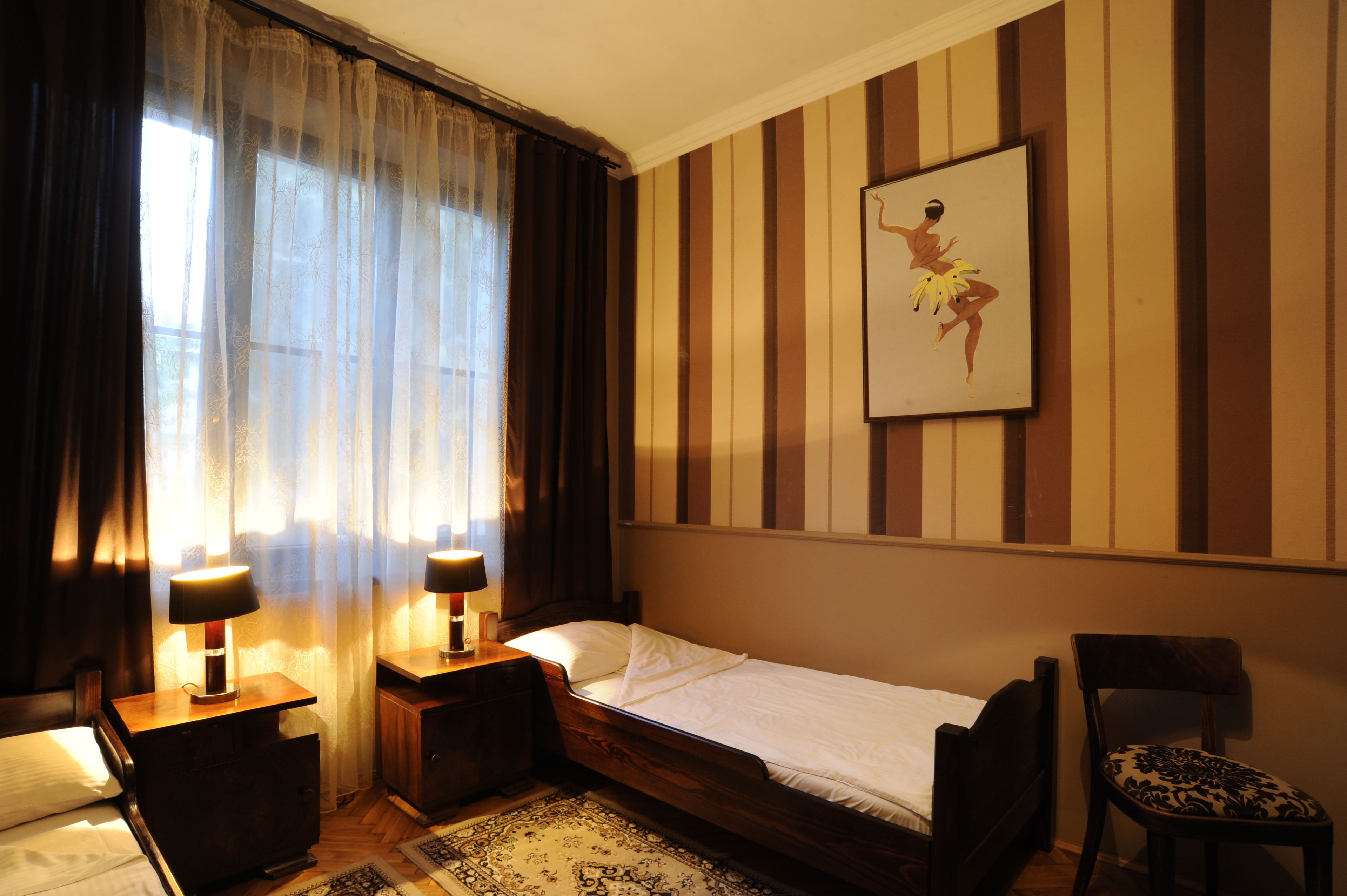 Une chambre d’hôtel avec un lit, deux lampes de chevet, une chaise, un tapis et un tableau accroché au mur.