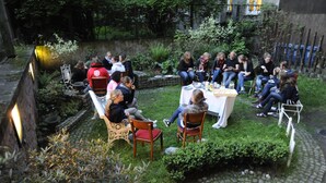 Un grupo de personas sentadas al aire libre en un jardín con muros de piedra y vegetación.
