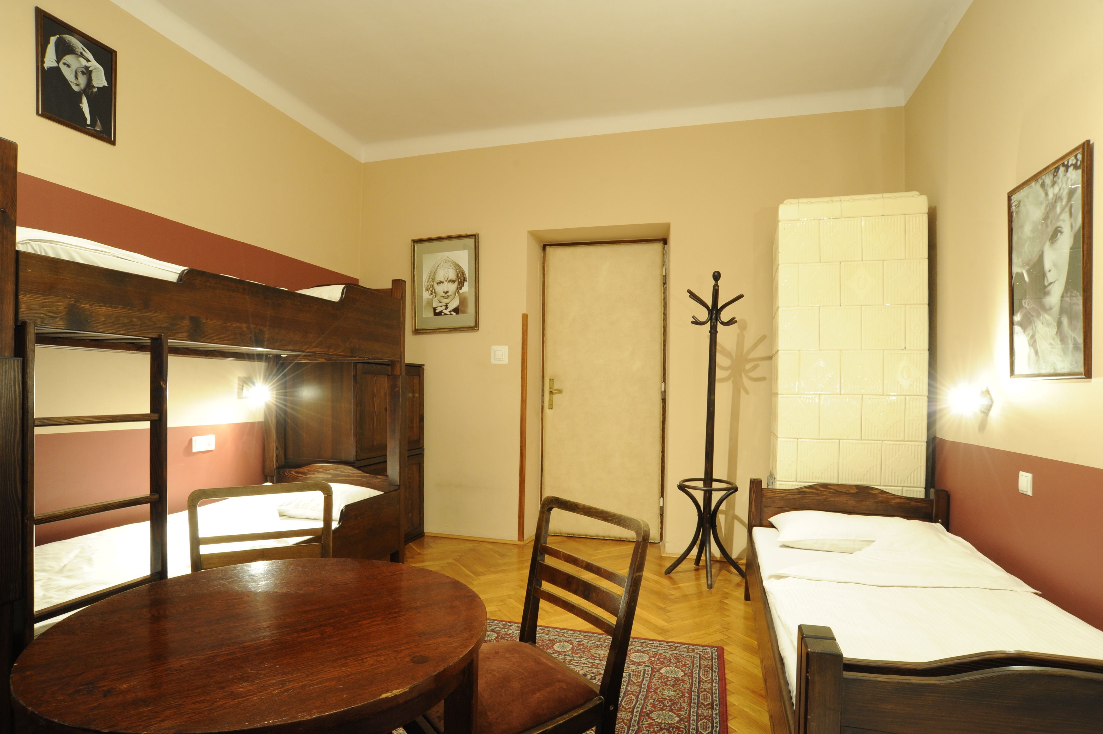 A room with a bunk bed, a single bed, a round wooden table, a chair, a coat rack, and a door.