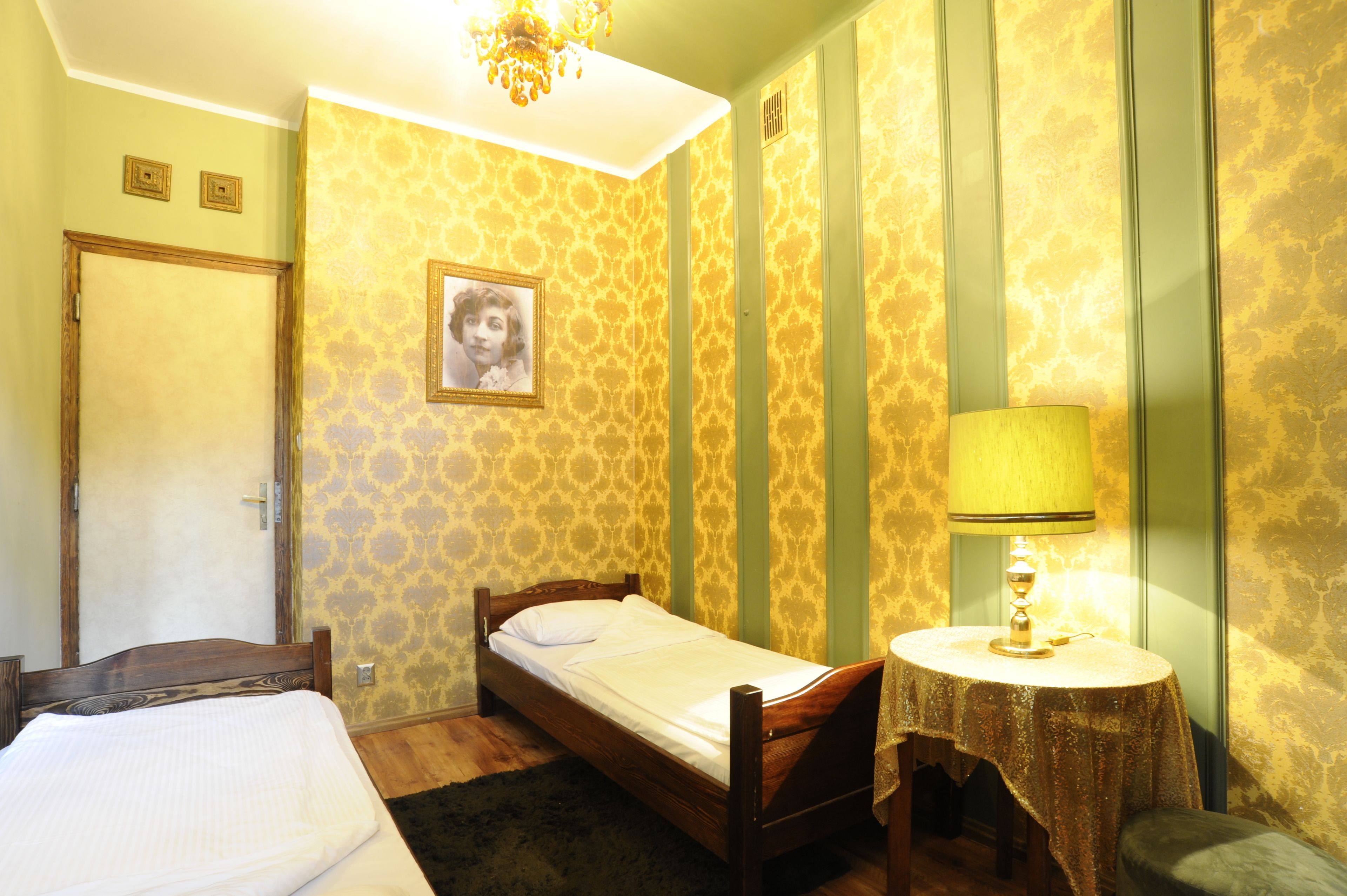 A small, cozy bedroom with a single bed, a bedside table with a lamp, and a door.