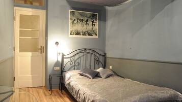 A bedroom with a bed, a bedside table, a wall-mounted picture, and a door.