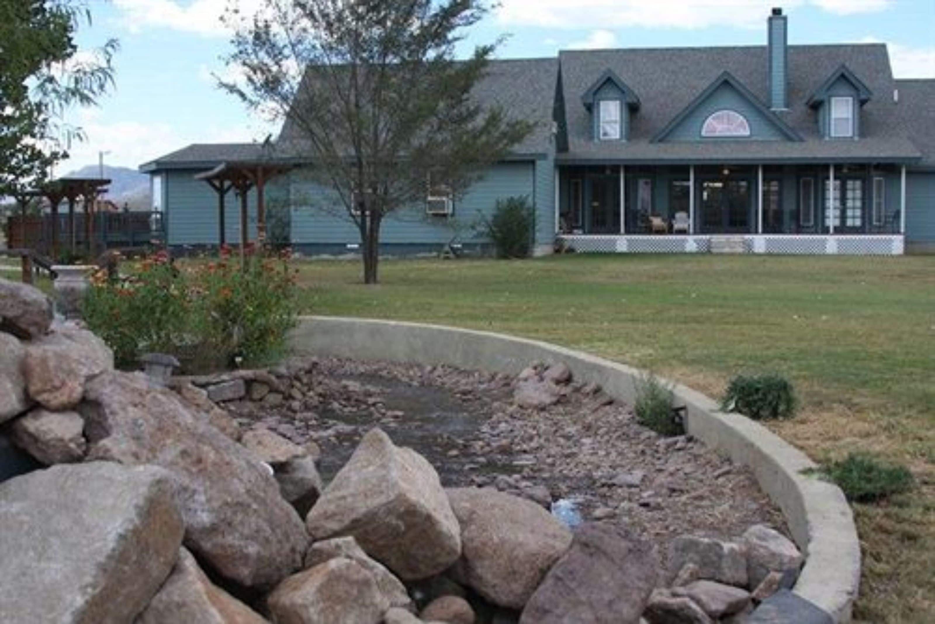 Un edificio con un porche, un muro de contención de piedra y un patio cubierto de césped.