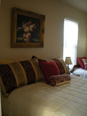 A bedroom with a large bed, a painting on the wall, and a window with blinds.