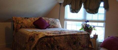 A bedroom with a bed, a window with curtains, and a nightstand with a plant.