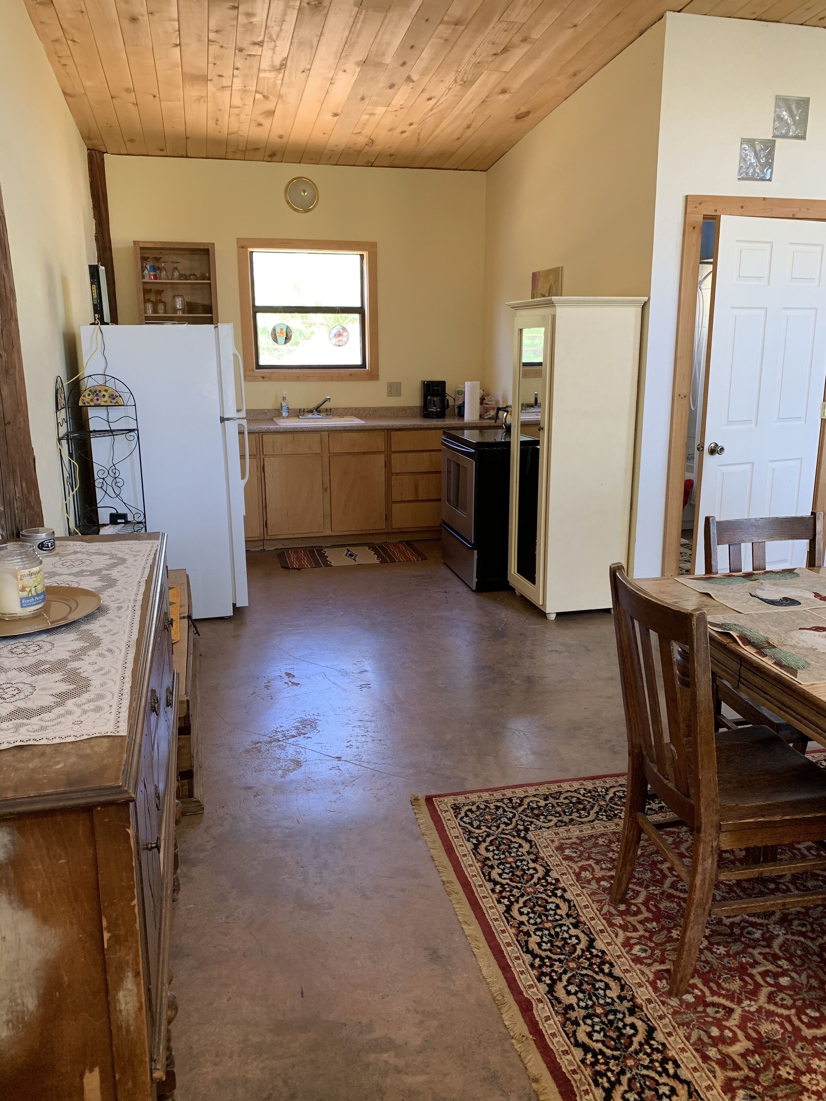 A compact kitchen with wooden cabinets, a refrigerator, a coffee maker, and a dining area with a table and chairs.