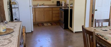 A compact kitchen with wooden cabinets, a refrigerator, a coffee maker, and a dining area with a table and chairs.