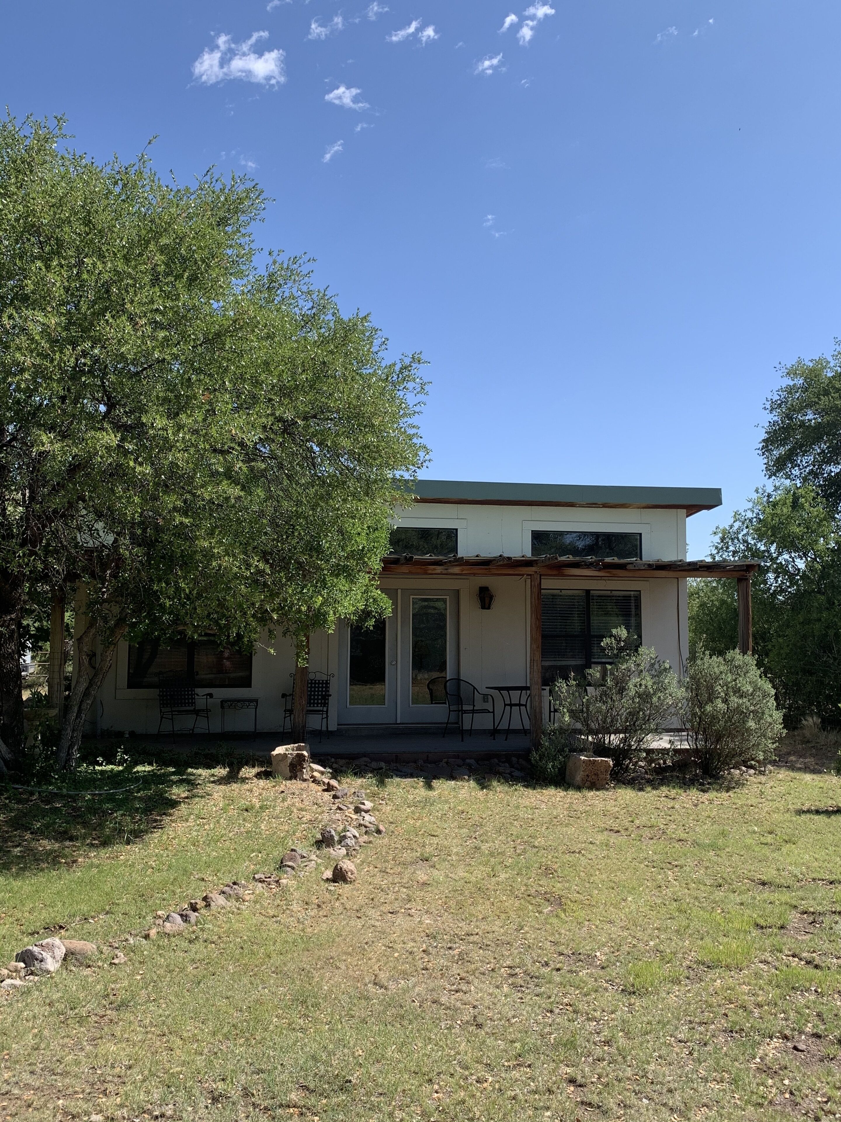 A two-story house with a covered porch, a small garden, and a large tree in front.
