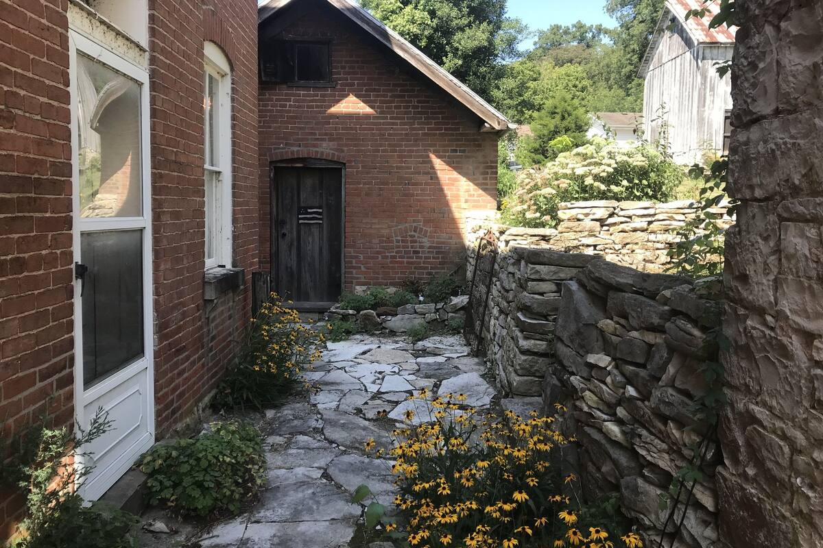 A narrow stone pathway leading to a brick house with a dark wooden door and a window with a white frame.