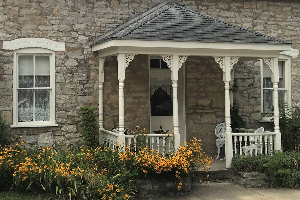 A stone building with a white porch and a small garden with yellow flowers.