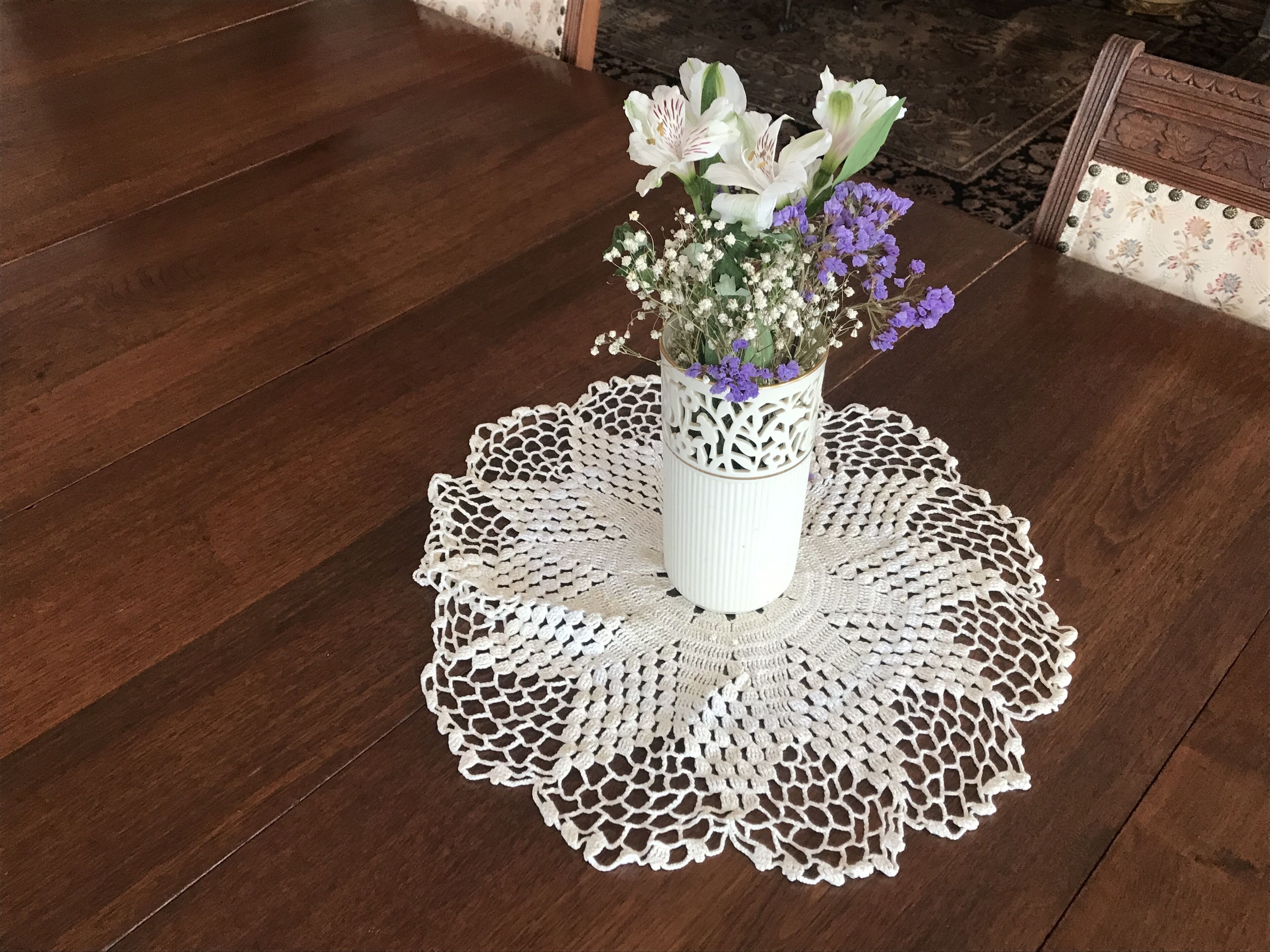Un jarrón blanco con flores sobre una mesa de madera con un mantel blanco.