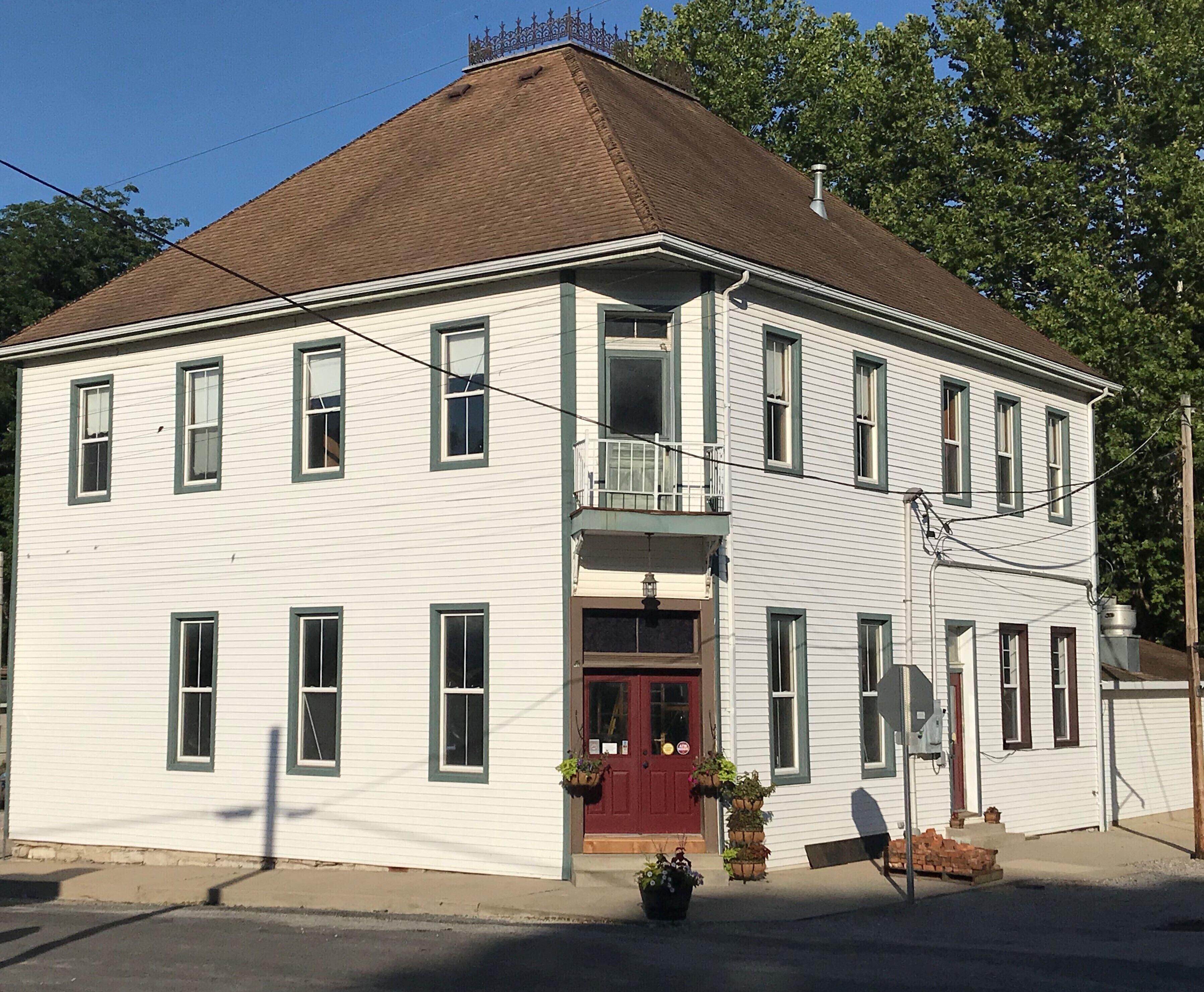 A two-story white building with a red door, multiple windows, and a small balcony.