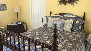 A bedroom with a floral-patterned bedspread, a wooden headboard, a bedside table with a lamp, and a door with a decorative wreath.