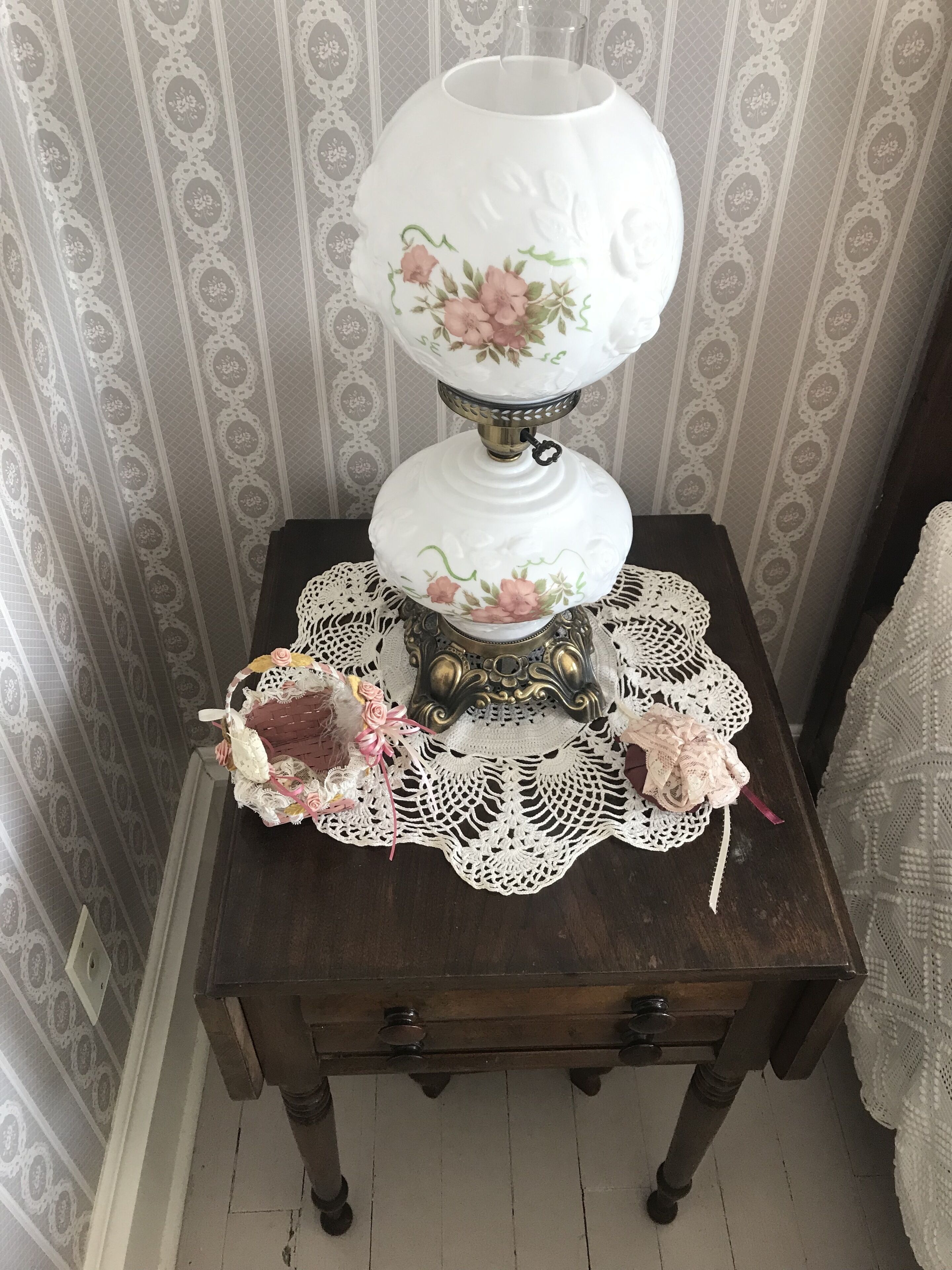 Une table ornée d’une lampe décorative, d’un chemin de table en dentelle et d’un panier rempli de fleurs.