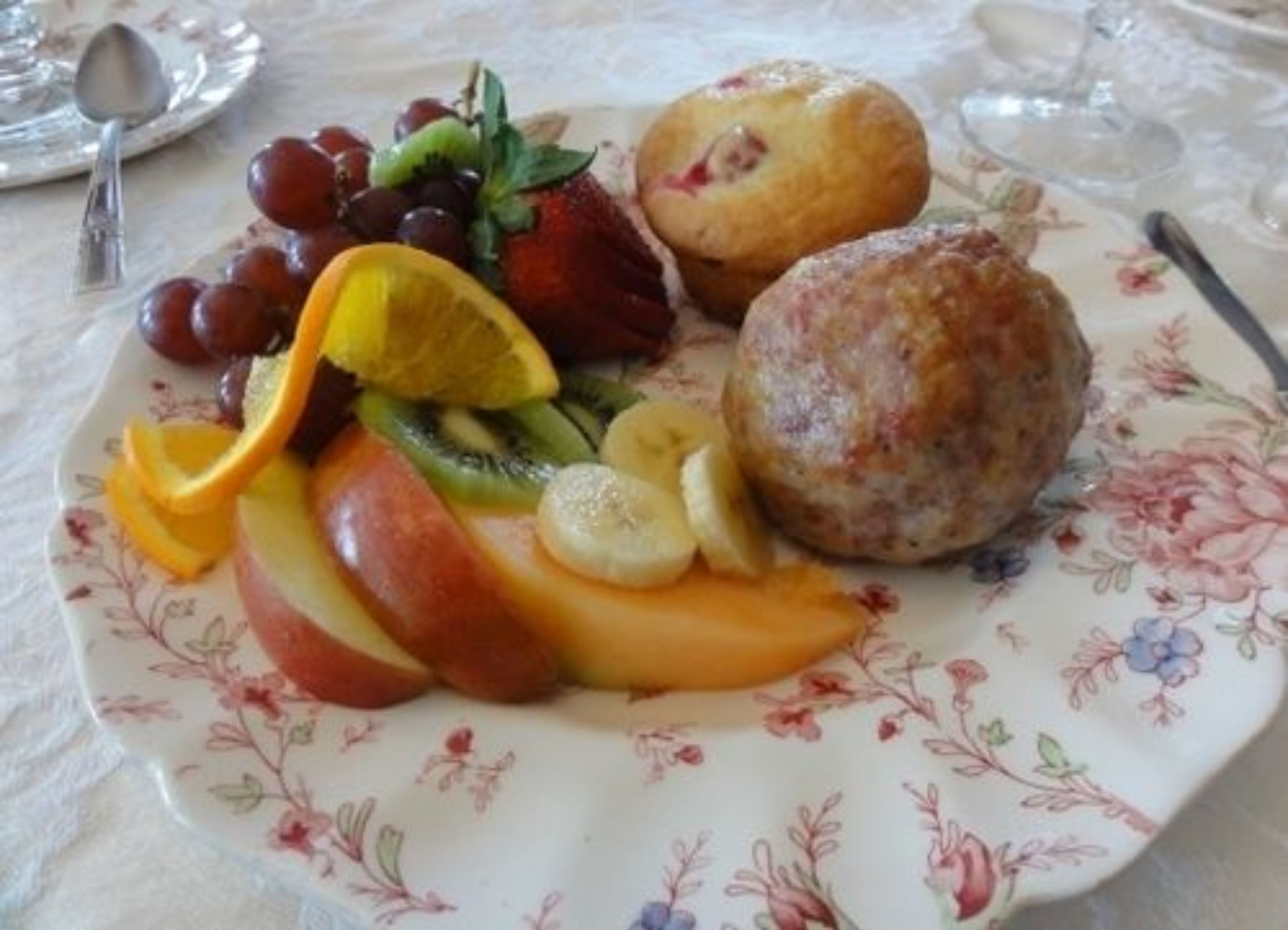 A plate with assorted fruits and two muffins on a floral-patterned plate.