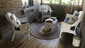 Un coin salon accueillant avec des fauteuils en osier et une table basse, un mur en briques et une fenêtre donnant sur un paysage verdoyant.