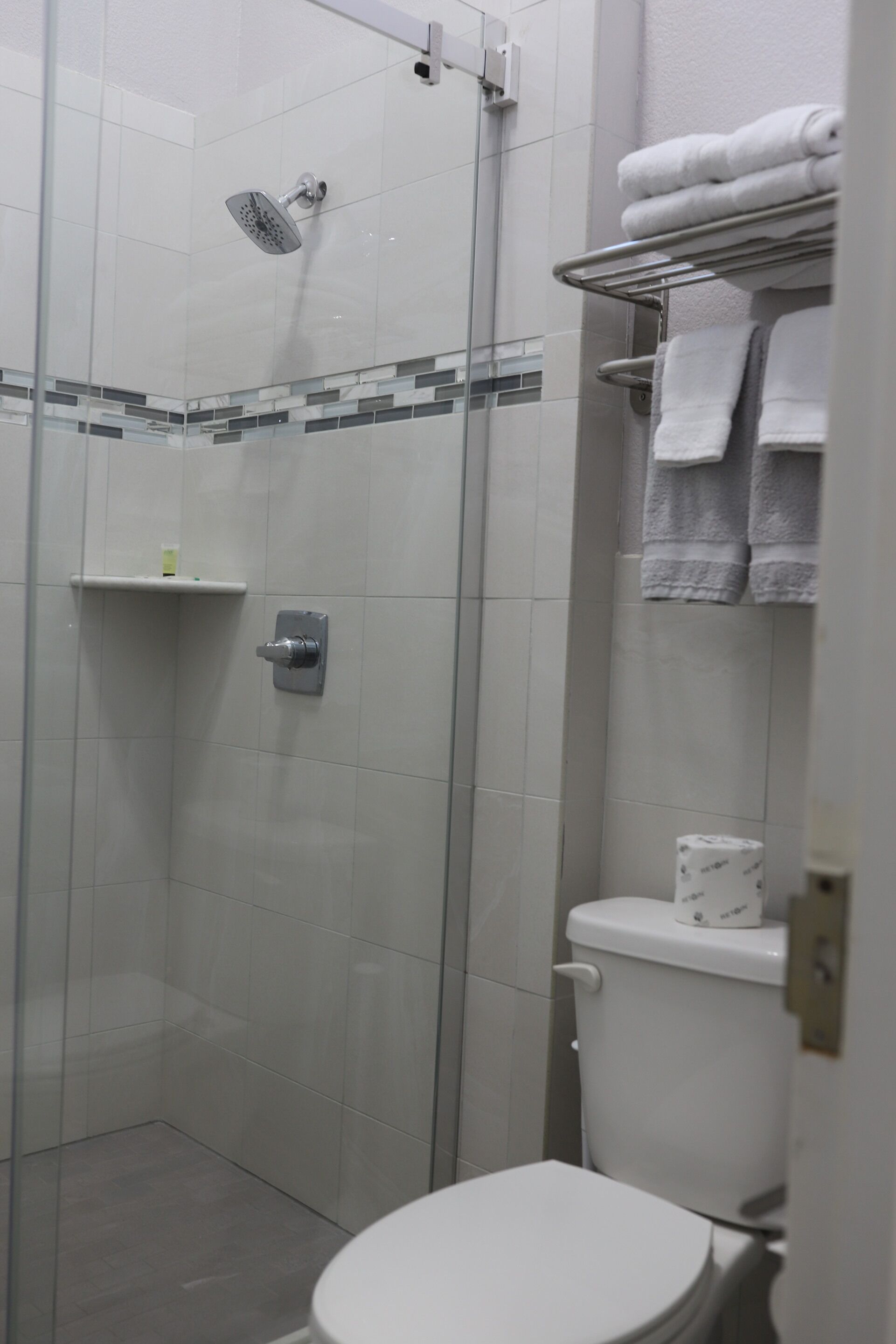 A modern bathroom with a glass-enclosed shower, a toilet, and a towel rack with folded towels.