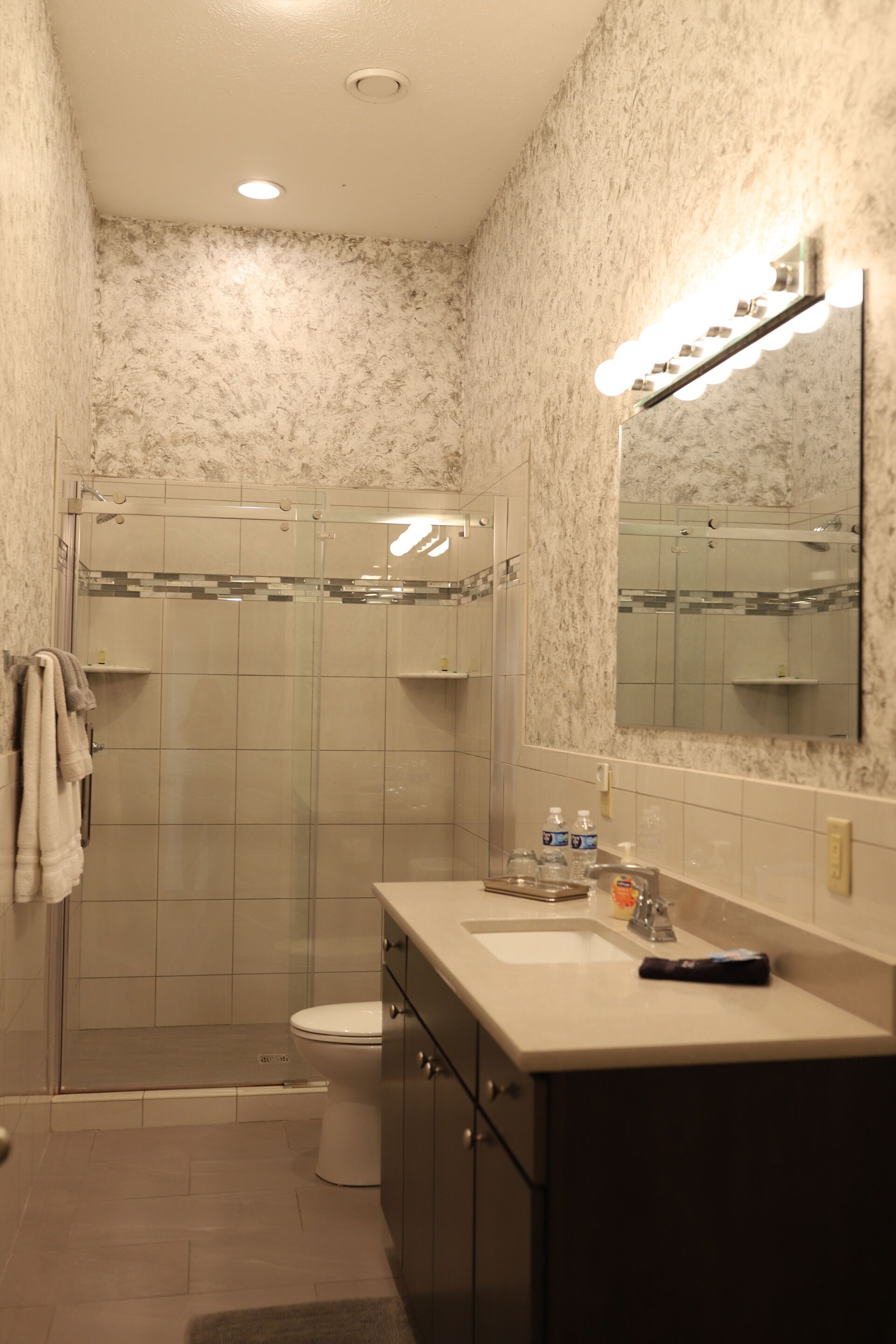A bathroom with a shower, toilet, sink, and mirror.