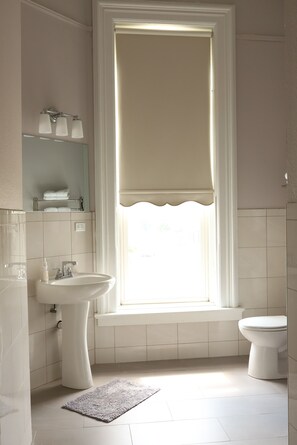 A bathroom with a sink, toilet, and window with a white curtain.