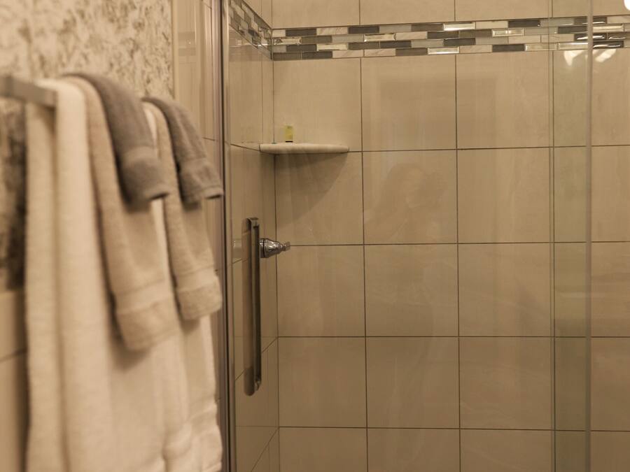 A glass-enclosed shower with a tiled wall and a towel rack with multiple towels.