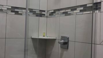 Un espace douche avec des murs carrelés, une porte en verre et un pommeau de douche.