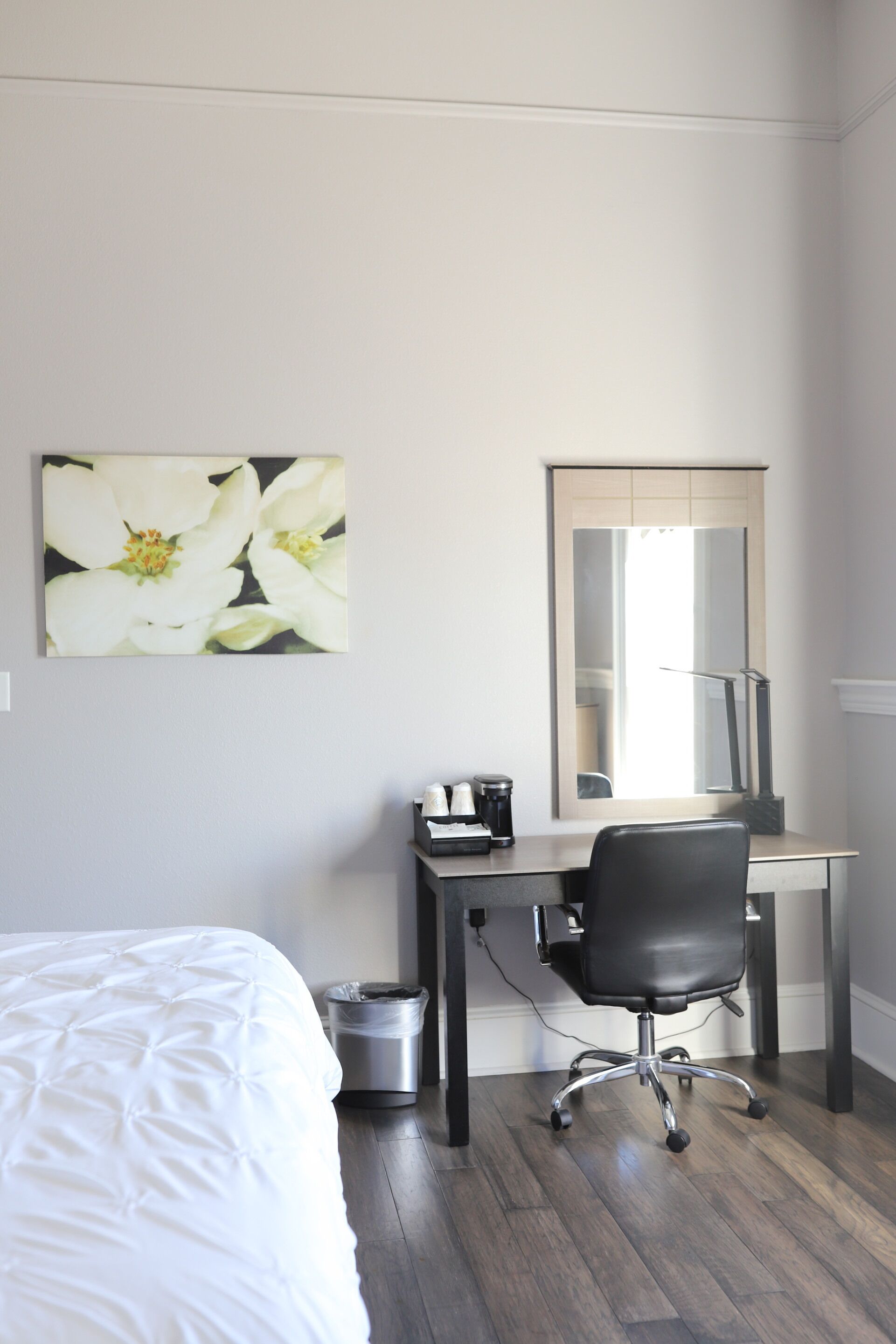 Une chambre d’hôtel comprenant un lit, un bureau avec une chaise, une poubelle et un grand miroir.