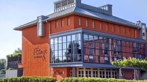 A modern building with a glass facade, a red exterior, and a sign that reads "Hotel". - Hotel Simon's Plaza (Grevenmacher)