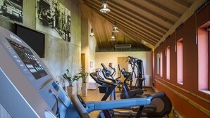 A gym with exercise equipment, wooden beams on the ceiling, and a wall-mounted screen. - Hotel Simon's Plaza (Grevenmacher)