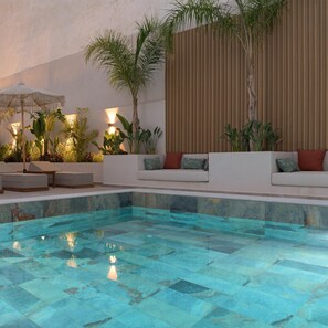 A swimming pool with a tiled deck, surrounded by seating areas with cushions and plants. - Sergios Hotel (Hersonissos)