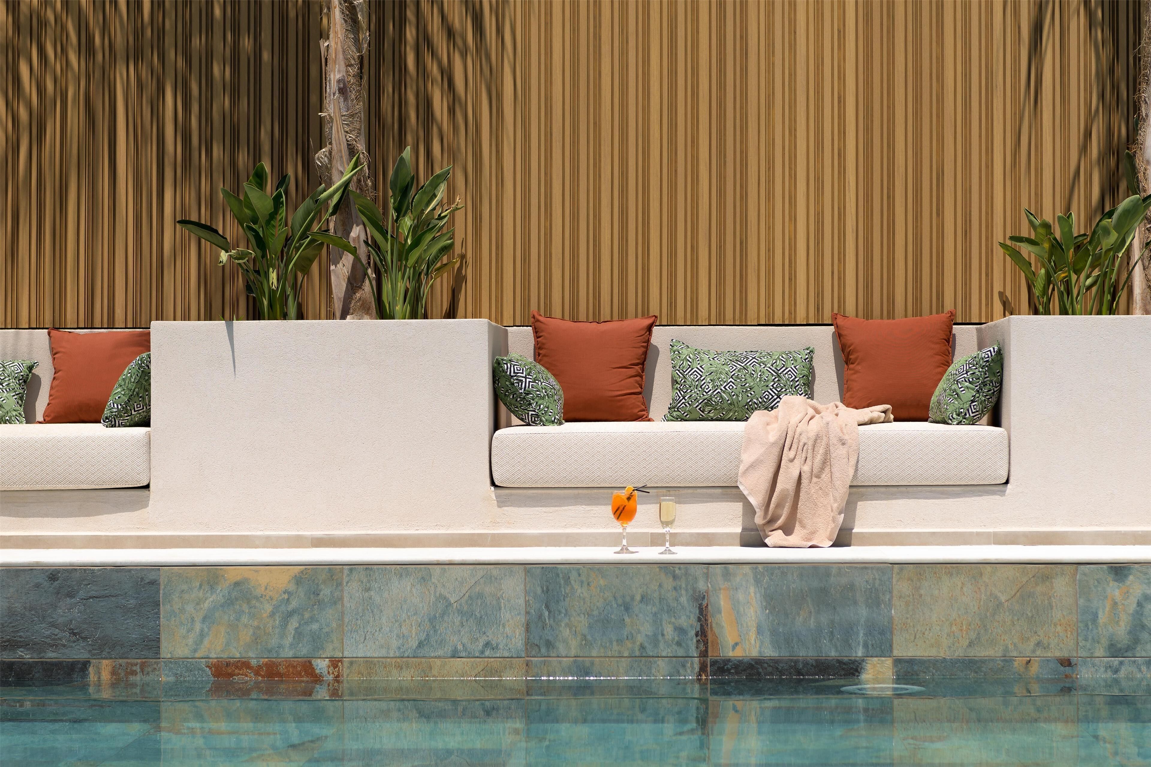 A poolside seating area with a tiled edge, two sofas with patterned cushions, and two potted plants.