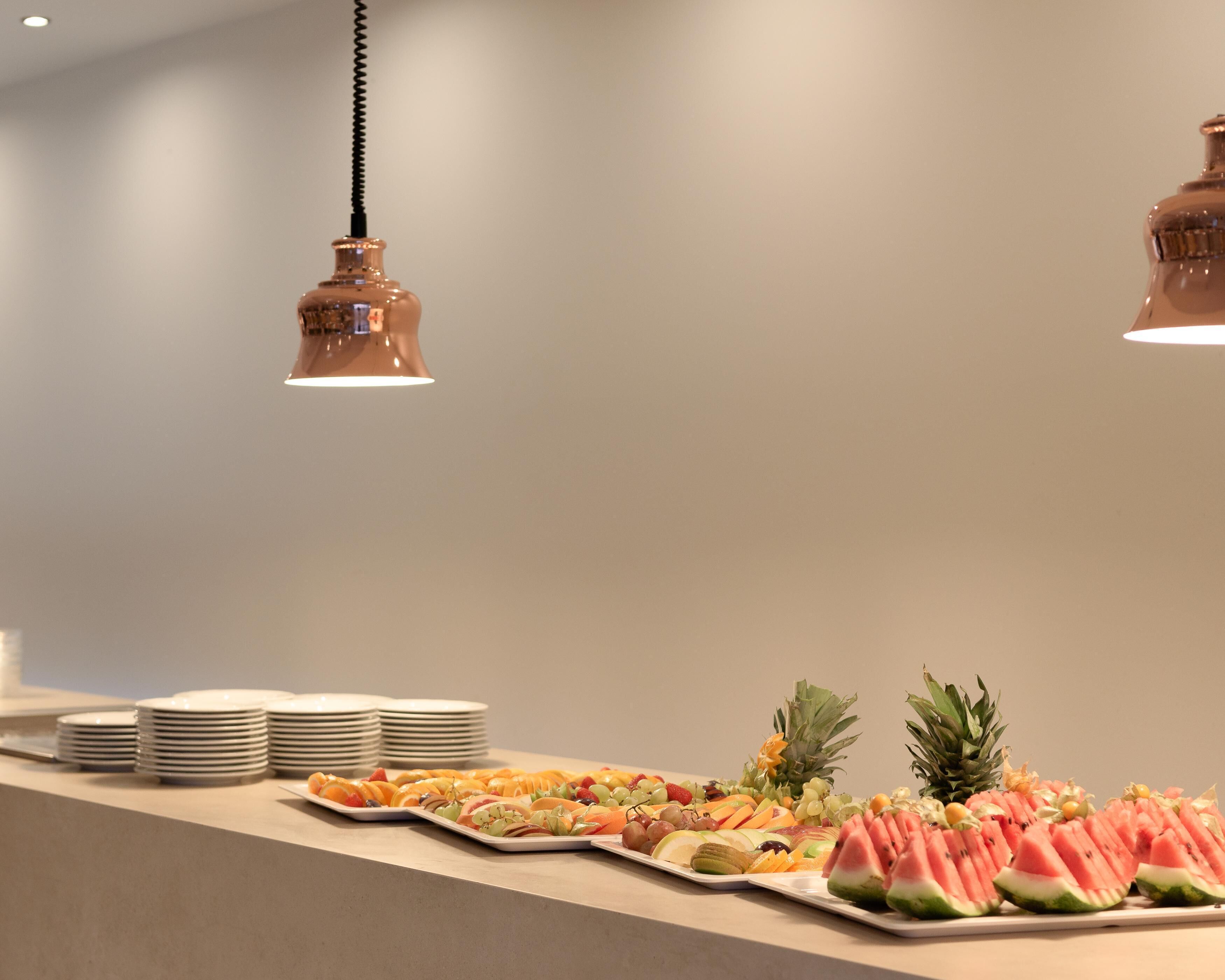 A buffet with various fruits and a stack of white plates.