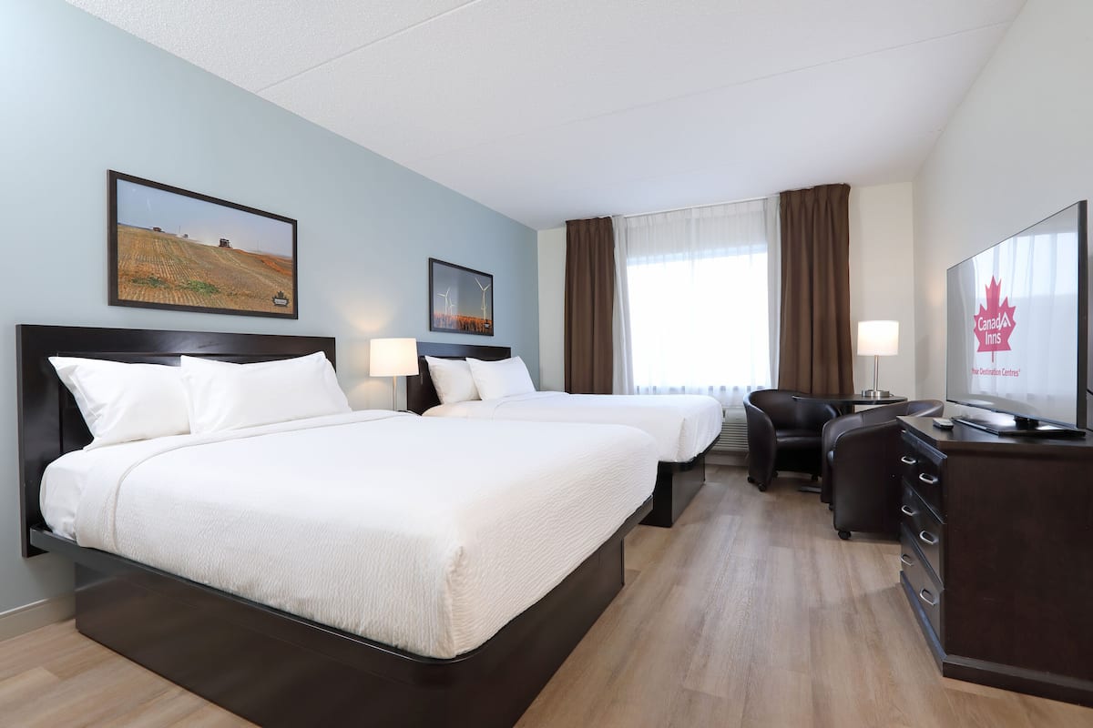 A hotel room with two beds, a desk, a chair, and a TV displaying the Canada Inn logo.