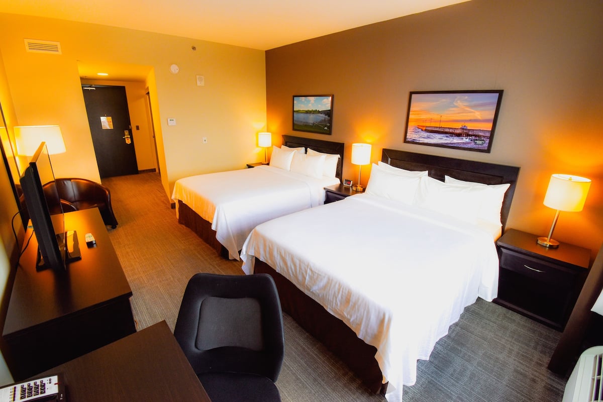 A hotel room with two beds, a desk, a chair, a TV, and two lamps.
