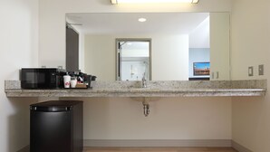 A modern bathroom with a granite countertop, a sink, a mirror, a trash bin, and a shower visible through the glass door. - Canad Inns Destination Centre Health Sciences Centre (Winnipeg)