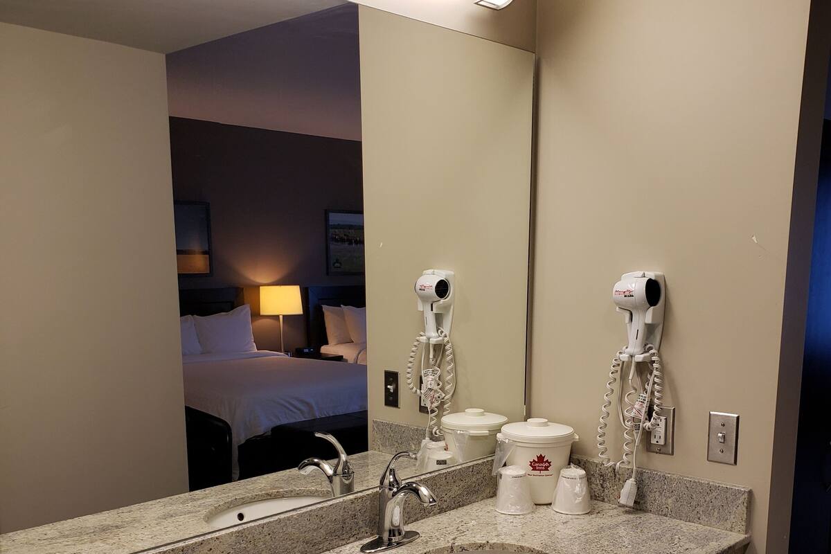 A hotel bathroom with a granite sink, a mirror, a hairdryer, and a cup holder.
