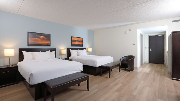 A hotel room with two beds, a bench, a chair, and two wall-mounted lamps. - Canad Inns Destination Centre Health Sciences Centre (Winnipeg)