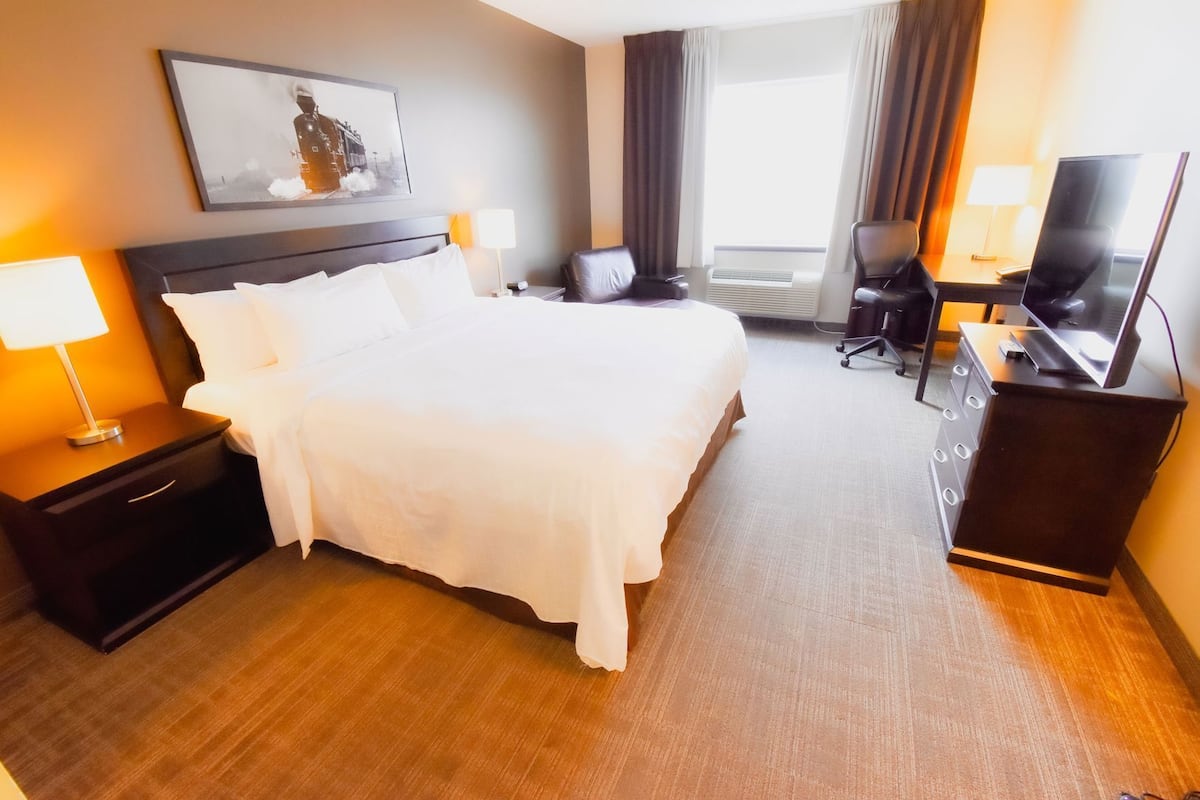 A hotel room with a large bed, bedside tables with lamps, a desk with a TV, and a chair.