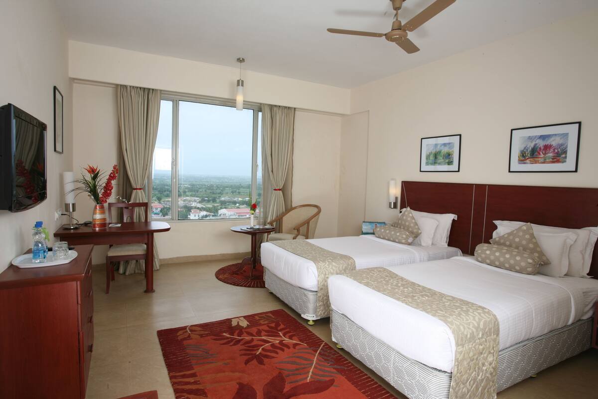 Une chambre d’hôtel avec deux lits, un bureau, une chaise et une vue sur la ville.