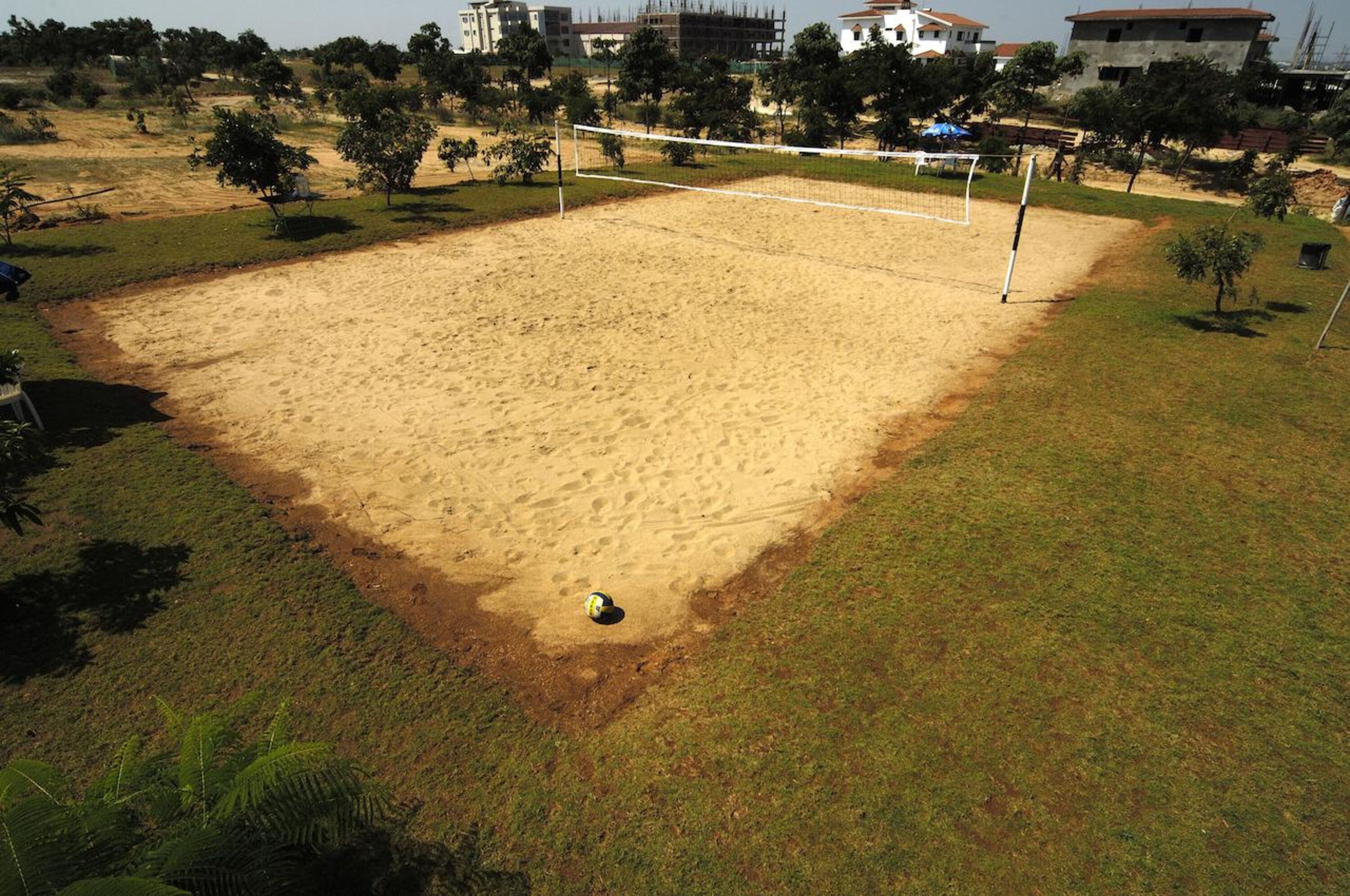 En sandvolleyballbane med net, omgivet af græs og træer.