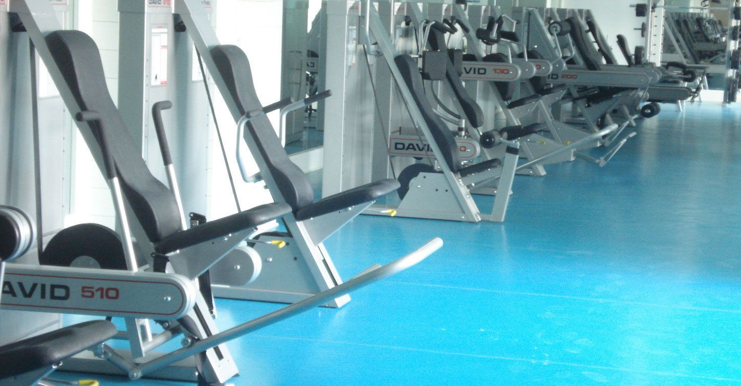 A row of stationary exercise machines in a gym with a blue floor.