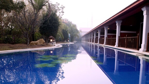 Una piscina con una estatua de león, rodeada de árboles y un paseo cubierto.