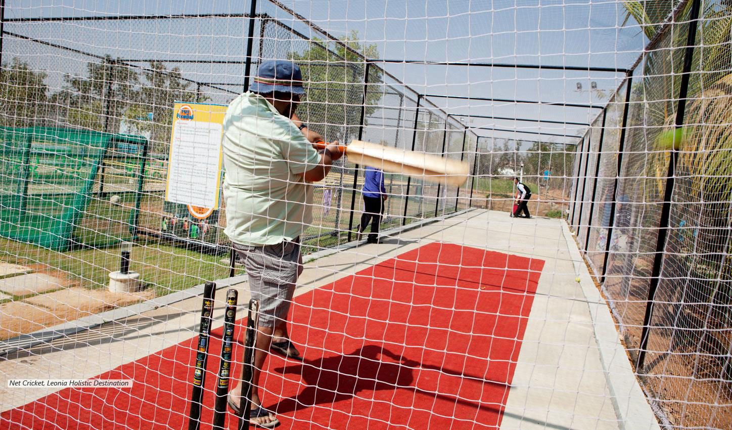 A net cricket practice area with a red mat, a batting cage, and a green storage unit.